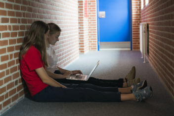 To elever der sidder med laptop på gangareal